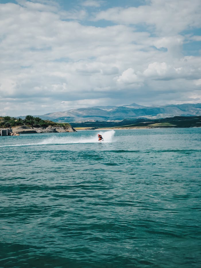 services-01 A person on a jetski enjoying a thrilling ride on open water surrounded by scenic mountains.