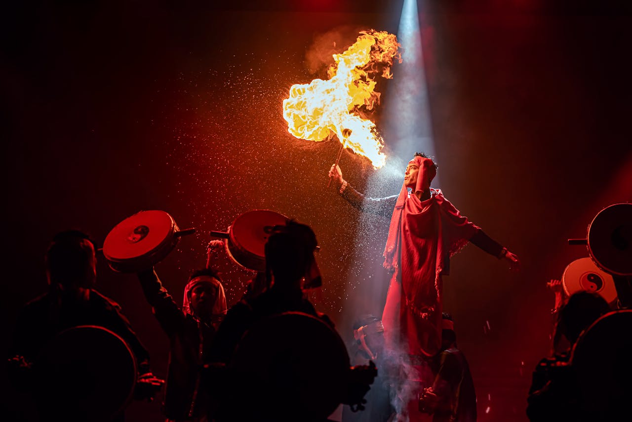 who-we-are A mesmerizing fire performer on stage surrounded by drummers in a dynamic, high-energy show.